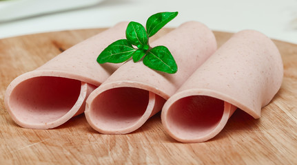 Slices of sausage on a wooden plate, and green leaf.