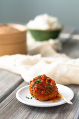 A classic beef meatball on a white ceramic plate served with a bamboo pick. Rice and cheesecloth in the background 