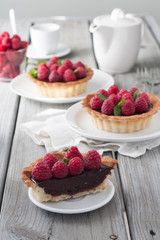 A weathered wood table with raspberry chocolate tarts and tea. Bright sun lit room. 