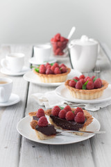 A weathered wood table with raspberry chocolate tarts and tea. Bright sun lit room. 