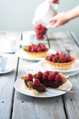 A weathered wood table with raspberry chocolate tarts and tea. Bright sun lit room. 