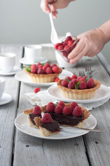 A weathered wood table with raspberry chocolate tarts and tea. Bright sun lit room. 