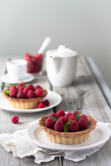 Chocolate tart with fresh raspberries and mint leaves, gray background . White ceramic teapot and cups in the background. 