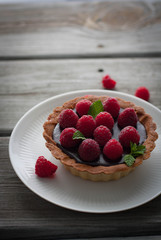 Chocolate tart with fresh raspberries and mint leaves, gray background 