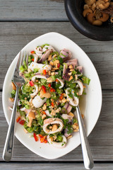 That style squid salad  in a white ceramic dish on a weathered wood table. 