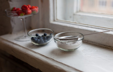 Blueberries strawberries icing sugar in a small bowl at the window
