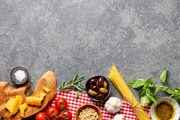 Fototapeta na wymiar Italian food ingredients background with raw spaghetti, olives, basil leaves, rosemary, parmesan cheese, garlic, pine nuts, olive oil and tomatoes.