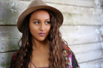 Pretty girl in a dress, flowered kimono and a hat standing up against an old wood wall