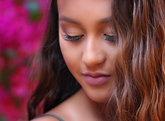 Naklejka premium Pretty, happy, long haired girl standing amongst some bougainvillea blossoms