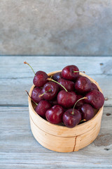 Sweet cherries in a bamboo basket. Weathered wood table and dark gray backdrop, isolated, minimalist. 