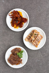 Assorted Asian appetizers on white plates:  octopus in spicy sauce, sliced beef shank, pigs ears. Dark gray background 