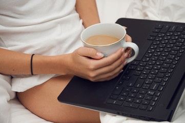 Woman sitting with laptop and a cup of coffee in a bed