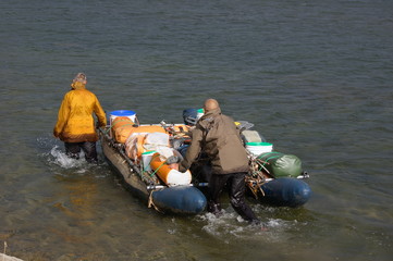 Two men travel up the river on an inflatable catamaran. Small Usa river, Polar Urals.