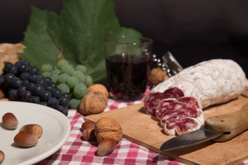Wineglass with red wine and sausage salame and fruits on black background