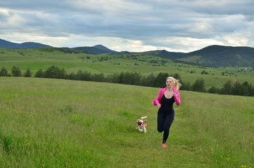 Lady in pink and black sportswear jogging with her dog in landscape on a cloudy day