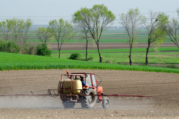 Tractor sprinkling pesticides against sugar beet bugs on plowed land on sunny spring day