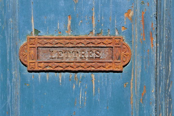 Traditional French rusty iron letter box on grungy blue flaky painted wooden door
