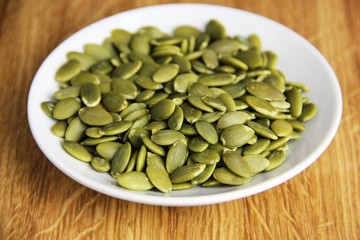 Pumpkin seeds on a white plate set on a white oak surface