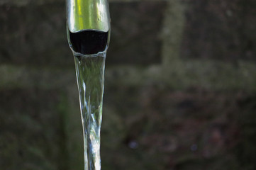 Close up of running water from a tap with brick wall in background