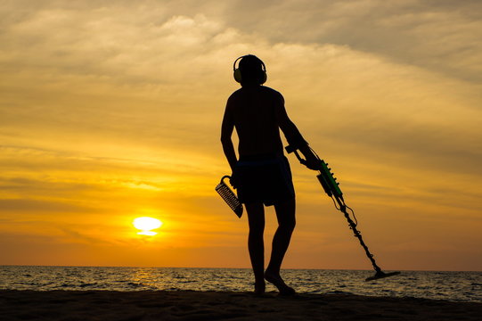 a treasure hunter with Metal detector on sunset on the beach