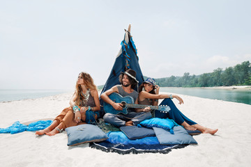Attractive boho man and women sitting on pillows at tepee