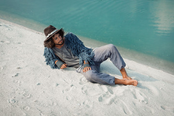 Attractive young gypsy man lying on sand at lake shore