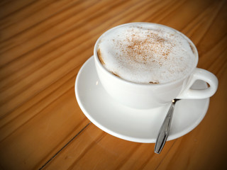Cappuccino coffee in white cup on wooden table in coffee shop.