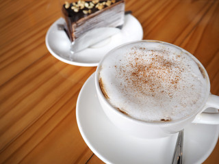Cappuccino coffee in white cup on wooden table in coffee shop.