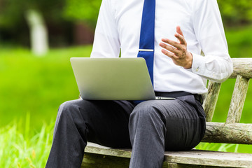 屋外でパソコン作業をしているビジネスマン 自然の緑背景