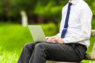 屋外でパソコン作業をしているビジネスマン 自然の緑背景