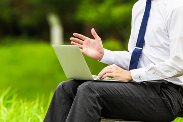 屋外でパソコン作業をしているビジネスマン 自然の緑背景