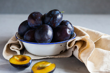 Plums in a bowl on a rural tablecloth on a gray background and half plums and plum stones on the table