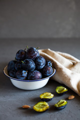 Plums in a bowl on a rural tablecloth on a gray background and half plums and plum stones on the table