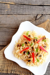 Pasta with red pepper, fried mushrooms and green onion. Vegetarian pasta on a plate isolated on old wooden background. Vegetarian food