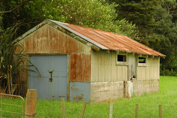 Shed made of rusty corrugated sheet metal on concrete base with gate and small windows.
