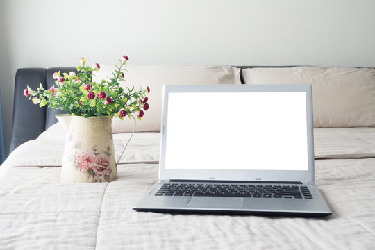 The bed with blank screen on laptop and mushroom flower on flower pot.