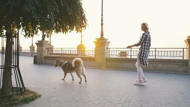 Young female walking with siberian husky dog on sea front at sunrise