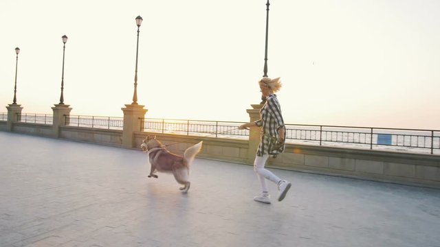 Young female walking with siberian husky dog on sea front at sunrise, slow motion