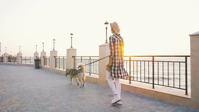 Young female walking with siberian husky dog on sea front at sunrise, slow motion