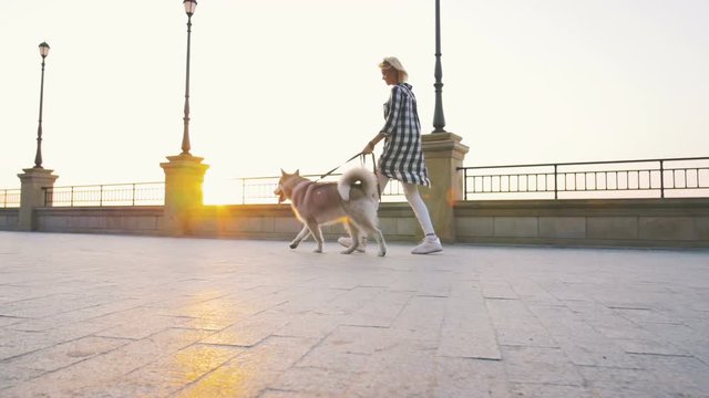 Young female walking with siberian husky dog on sea front at sunrise, slow motion