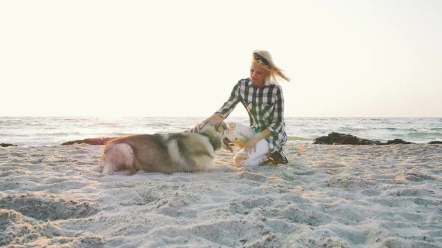 Young female playing with siberian husky dog on the beach at sunrise, slow motion