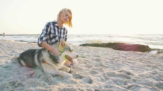 Young female putting sungglasses on siberian husky dog on the beach,slow motion