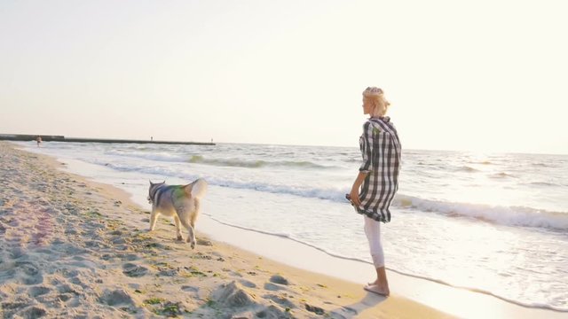 Young female running with siberian husky dog on the beach at sunrise,slow motion