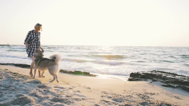 Young female running and playing with siberian husky dog on the beach at sunrise,slow motion