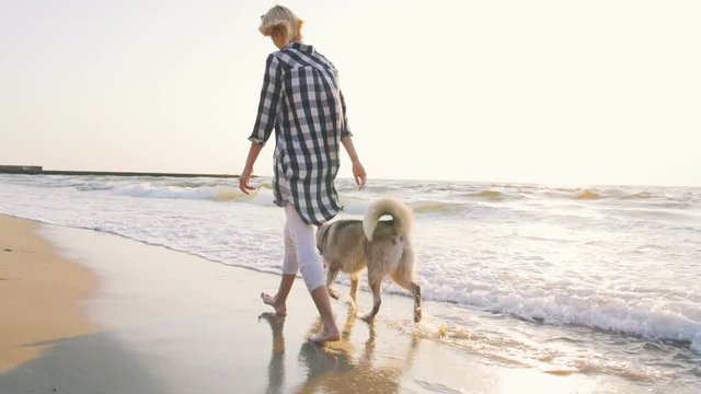 Young female walking and playing with siberian husky dog on the beach at sunrise,slow motion