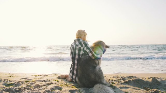 Young female hugging with siberian husky dog on the beach at sunrise, slow motion
