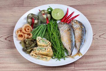 Ready side dish of deep fired mackarel,vegetable omelet,crispy pork rind,pickle lettuce,halve green lemon,red chili and boiled of eggplant,lentils,acacia  on wood. Side view