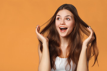 Surprised happy beautiful woman looking sideways in excitement. Isolated on orange background