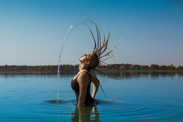 Junge Frau mit Tanktop steht in See und wirft nasse Haare in den Nacken