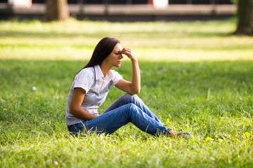 Beautiful businesswoman is sitting at the park and she is having a strong headache.
